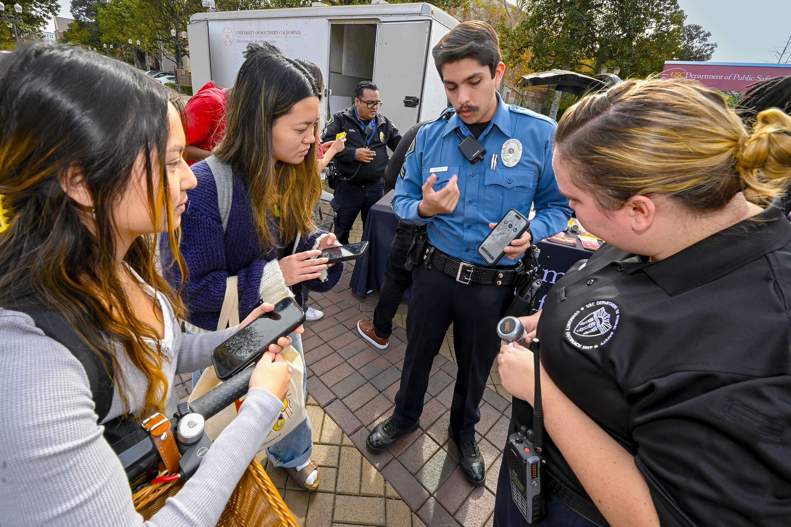 USC Department of Public Safety officers demonstrate a safety device to students using their phones at an outdoor event.